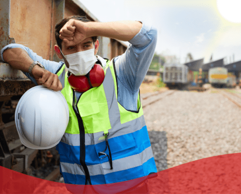 worker wiping his forehead in the heat outdoors wearing a hi-vis, mask and ear defenders around his neck.