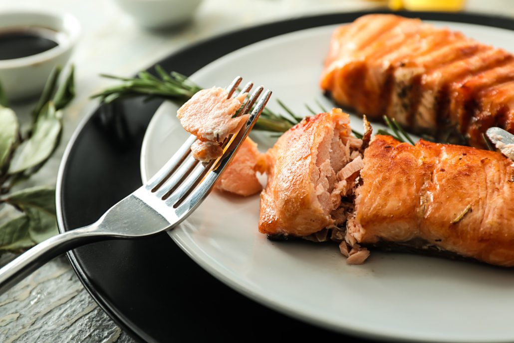 a fork with salmon on it with a pan fried salmon on a plate in the background