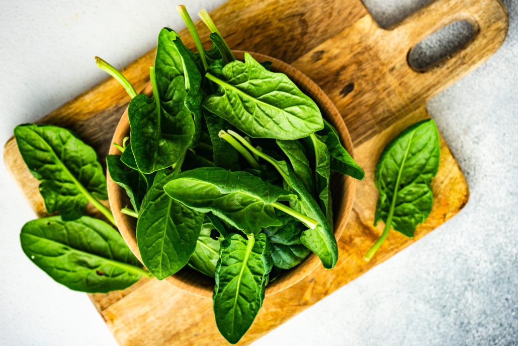 Spinach in a bowl on a wooden chopping board.